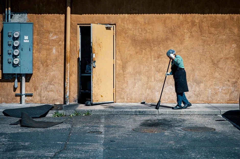 A person is cleaning a floral rug indoors using a yellow vacuum cleaner.